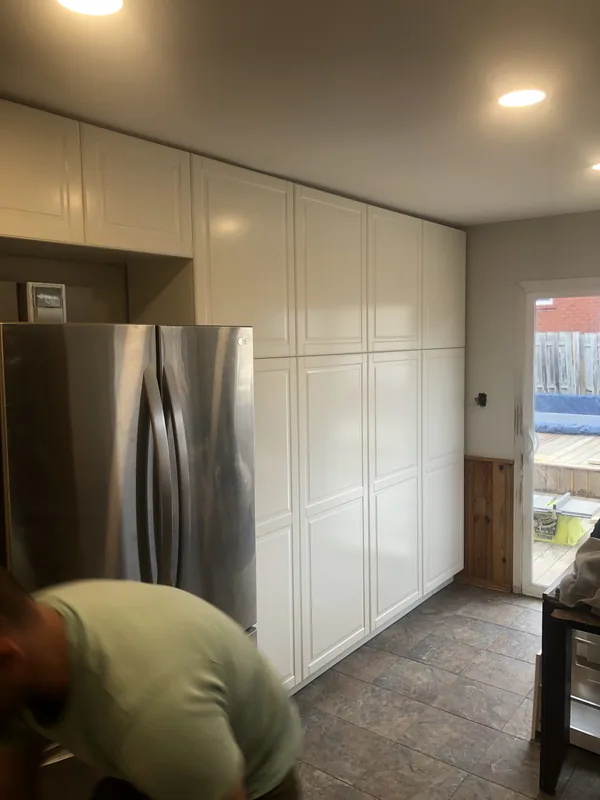 Floor to ceiling white pantry cabinets beside a refrigerator