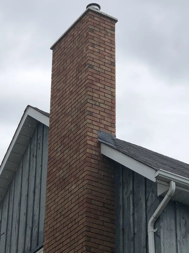 Rebuilt brick chimney rising through the roofline of a board and batten house