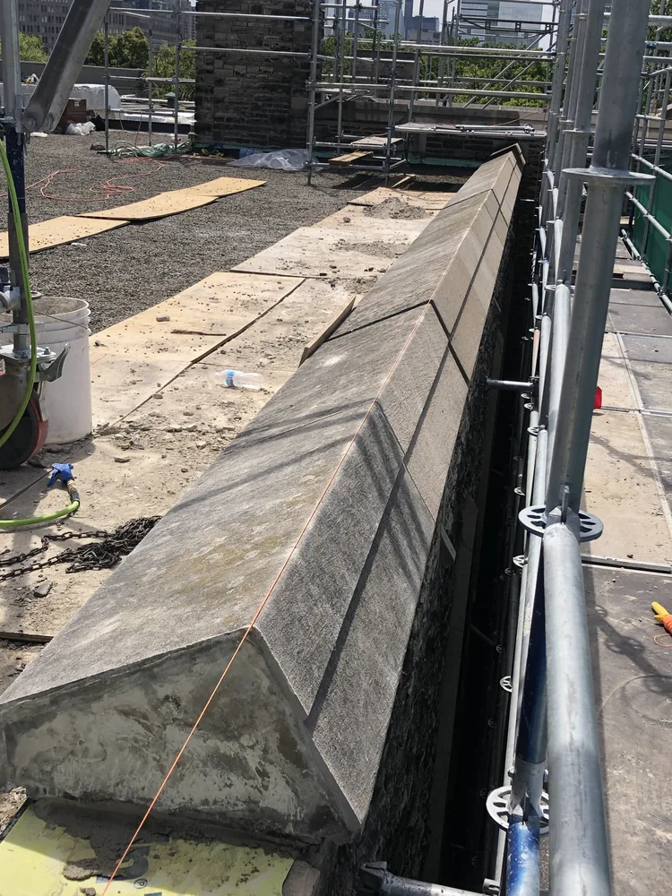 New stone parapet coping set on a commercial rooftop behind scaffolding