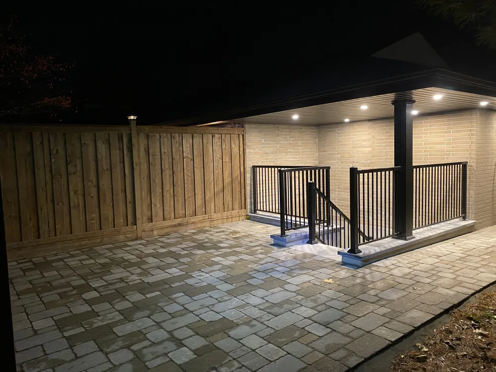 Lit paver patio and railed walkout stairwell under a covered porch at night